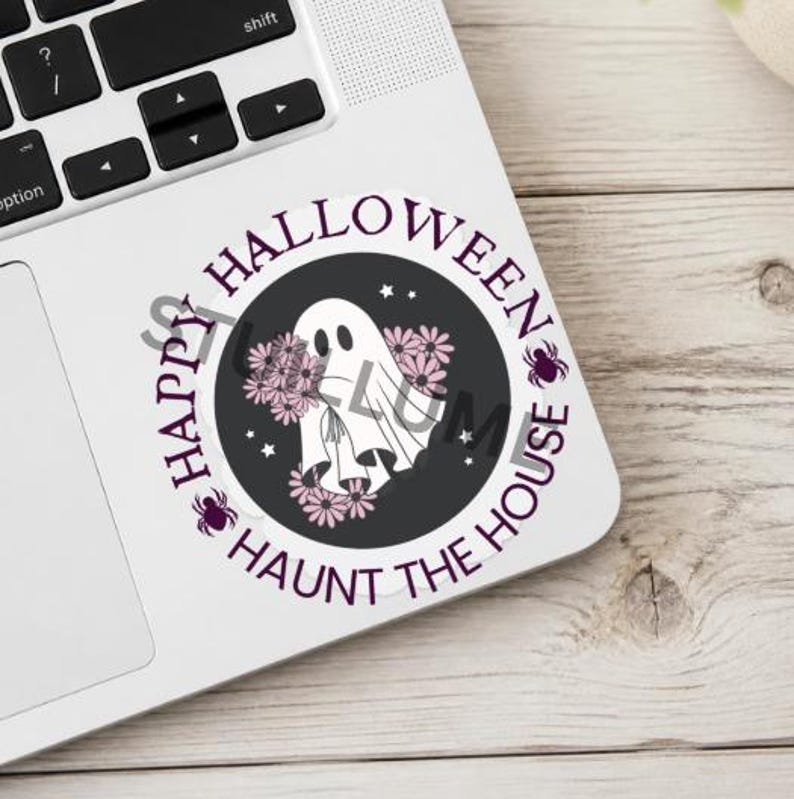 Puede incluir: Una pegatina circular con un fantasma blanco rodeado de flores rosas sobre un fondo gris oscuro. El texto "HAPPY HALLOWEEN" y "HAUNT THE HOUSE" est&aacute; impreso en morado alrededor del borde, con peque&ntilde;as estrellas y dos ara&ntilde;as moradas.