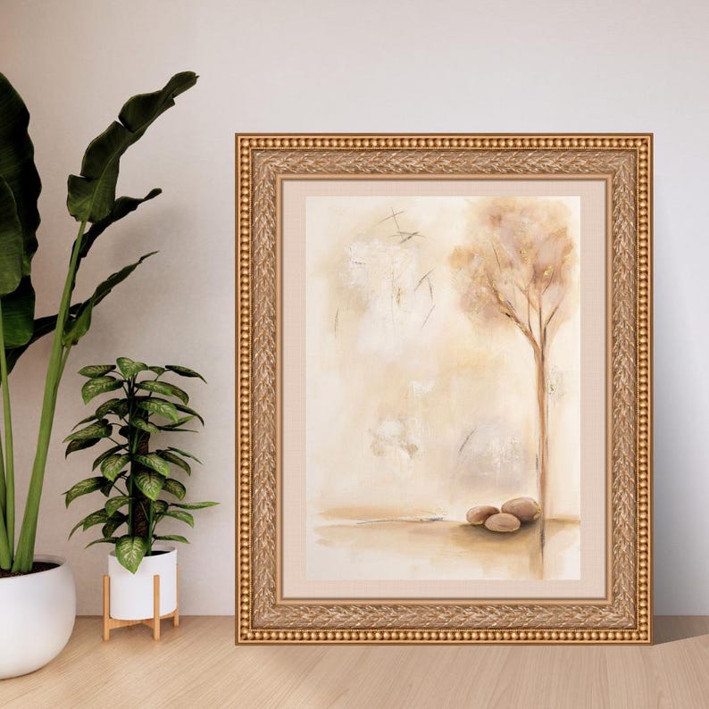 K&ouml;nnte beinhalten: Ein gerahmtes Wandbild mit einem abstrakten Aquarellgem&auml;lde eines einzelnen Baumes und drei glatten Steinen in Beige-, Creme- und Braunt&ouml;nen. Das Kunstwerk befindet sich in einem verzierten, strukturierten Goldrahmen mit einem breiten, neutralen Passepartout.