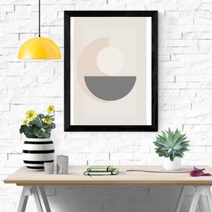Può includere: Una stampa artistica astratta incorniciata con una cornice nera. L'opera presenta un design geometrico con un semicerchio grigio, un cerchio bianco e uno sfondo beige. Una lampada a sospensione gialla è appesa sopra una scrivania di legno con un vaso di fiori e una succulenta.