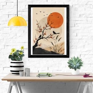 K&ouml;nnte beinhalten: Ein gerahmter Wandkunstdruck mit der schwarzen Silhouette eines bl&uuml;henden Baumzweigs mit zwei darauf sitzenden V&ouml;geln vor einem Hintergrund aus einer gro&szlig;en orangefarbenen Sonne, einem blassen Mond, fernen Bergen und fliegenden V&ouml;geln.