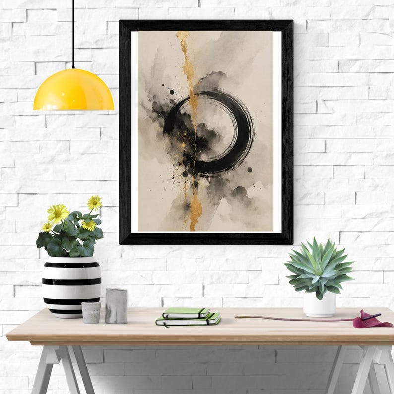 Op de afbeelding: Een ingelijste wandkunstprint met een abstract aquarelontwerp met een opvallende zwarte cirkelvormige penseelstreek, een verticaal bladgoudaccent en donkere inktspatten op een neutrale beige achtergrond, geplaatst in een eenvoudige zwarte lijst.