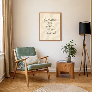 May include: A framed print with the text "Dreams are better when shared" hangs above a green armchair with a patterned pillow. A wooden side table holds a potted plant. A black lamp stands nearby.