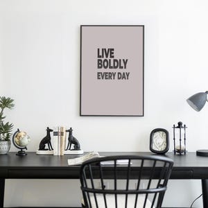 May include: A modern home office setup with a black desk, chair, and accessories. A framed print with the text "LIVE BOLDLY EVERY DAY" hangs above the desk. Decorative items include a potted plant, globe, bookends, and a desk lamp.