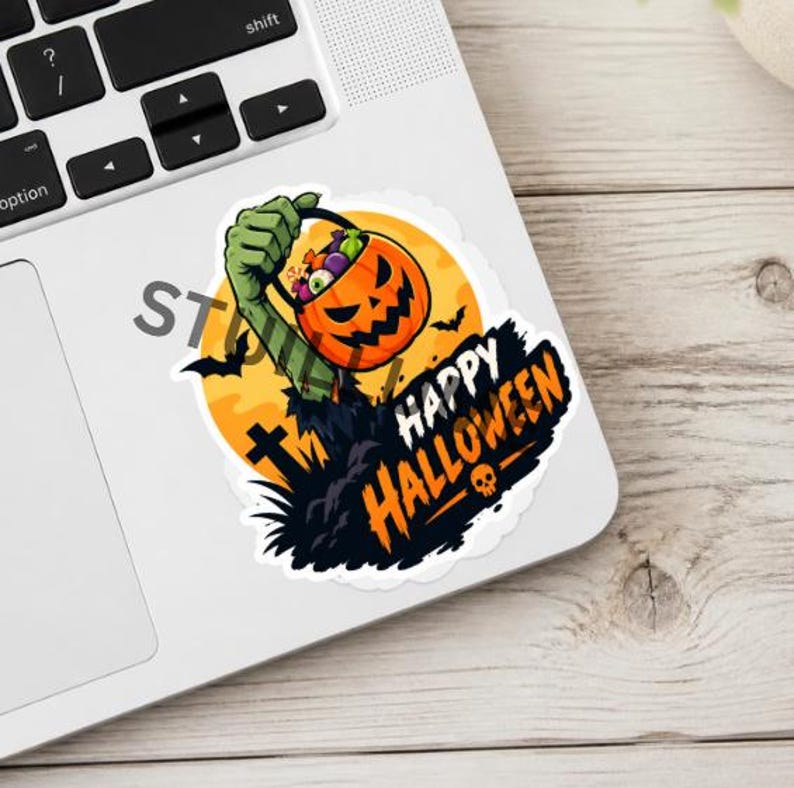 Puede incluir: Una pegatina troquelada que muestra una mano de zombi verde emergiendo del suelo, sosteniendo un cubo de caramelos naranja con forma de calabaza. El dise&ntilde;o incluye una luna amarilla, murci&eacute;lagos negros, una l&aacute;pida y el texto HAPPY HALLOWEEN.