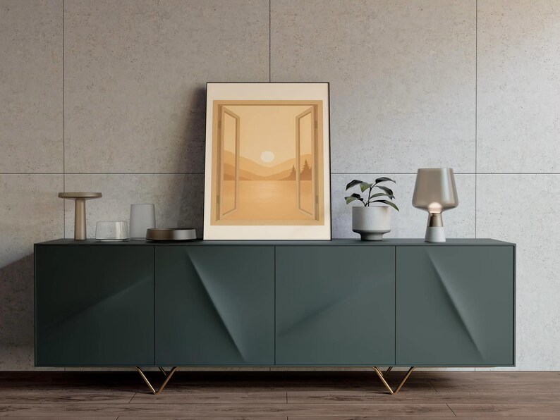 May include: A dark teal modern sideboard with gold legs, holding a framed landscape art print. A small potted plant and a table lamp are on the sideboard. The art print depicts a sunset scene with an open window.