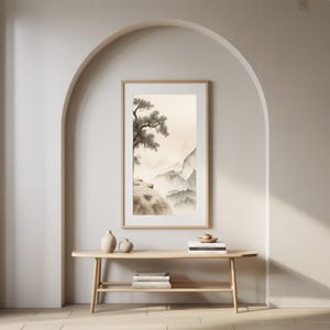 Può includere: Una stampa artistica incorniciata di un paesaggio con un albero su una scogliera che domina una catena montuosa nebbiosa. L'opera d'arte è in tenui tonalità di grigio, beige e marrone, con una cornice di legno. La stampa è esposta sopra una consolle in legno.