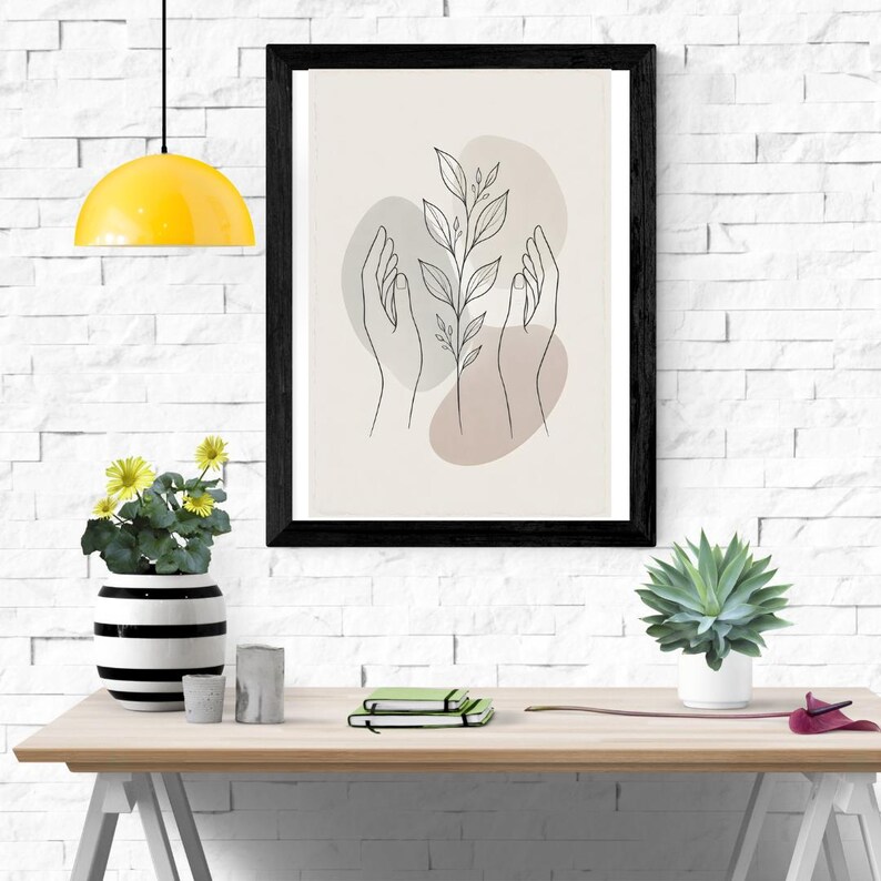 Pu&ograve; includere: Una stampa artistica da parete incorniciata con un disegno a linee nere di due mani che avvolgono un gambo di pianta centrale con foglie. Il design &egrave; su uno sfondo beige chiaro con morbide forme astratte grigie e marroni dietro le mani.