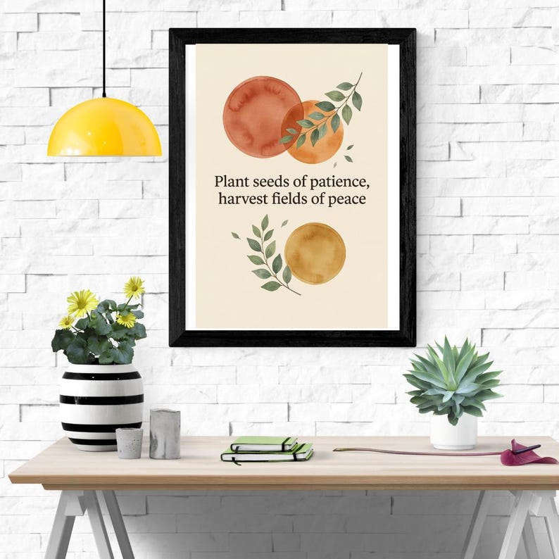 May include: A framed wall art print featuring a cream background with watercolour circles in shades of orange and gold, green leaf illustrations, and the black text: Plant seeds of patience, harvest fields of peace. The frame is black.