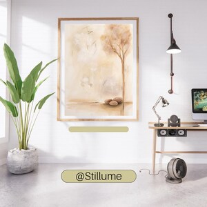 K&ouml;nnte beinhalten: Ein gerahmter Wandkunstdruck mit einer abstrakten Landschaft in Beige- und Braunt&ouml;nen, die einen einzelnen Baum und drei Steine am Boden zeigt. Das Bild h&auml;ngt an einer wei&szlig;en Wand neben einer gr&uuml;nen Topfpflanze, einer Schreibtischlampe und einem Monitor.