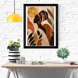 May include: A framed wall art print featuring a profile illustration of a person wearing a patterned headwrap and a large gold hoop earring. The artwork displays a warm colour palette of gold, terracotta, and cream with abstract botanical shapes.