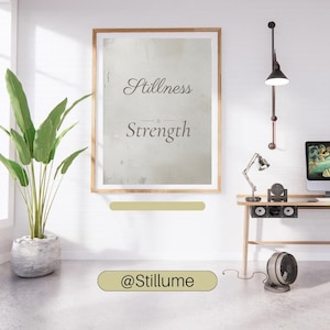 May include: A framed print featuring the words "Stillness Strength" in a stylish font. The image is set in a contemporary interior with a desk, plant, and industrial lighting. The text "@Stillume" is also visible.