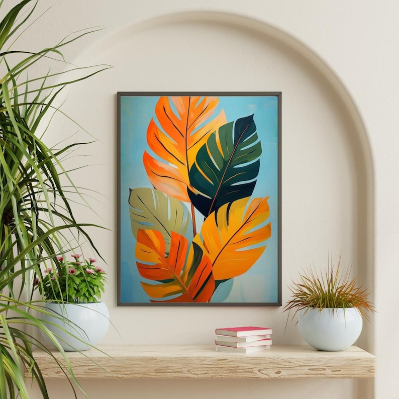 Pu&ograve; includere: Una stampa artistica incorniciata con foglie tropicali stilizzate nei toni dell'arancione, giallo, verde e verde oliva su uno sfondo azzurro. L'opera d'arte &egrave; esposta su una mensola di legno con piante in vaso e libri.
