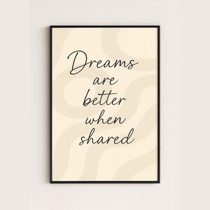 May include: A framed art print with the quote "Dreams are better when shared" in black script. The background is a light beige with wavy, cream-colored accents. The frame is black.