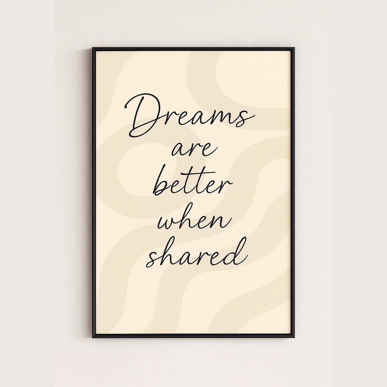 May include: A framed art print with the quote "Dreams are better when shared" in black script. The background is a light beige with wavy, cream-colored accents. The frame is black.