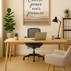 May include: A light wood desk with a laptop, black desk lamp, and a framed print that reads "Choose peace over pressure." A black office chair and a beige armchair are also present. Potted plants and a mug complete the office setting.
