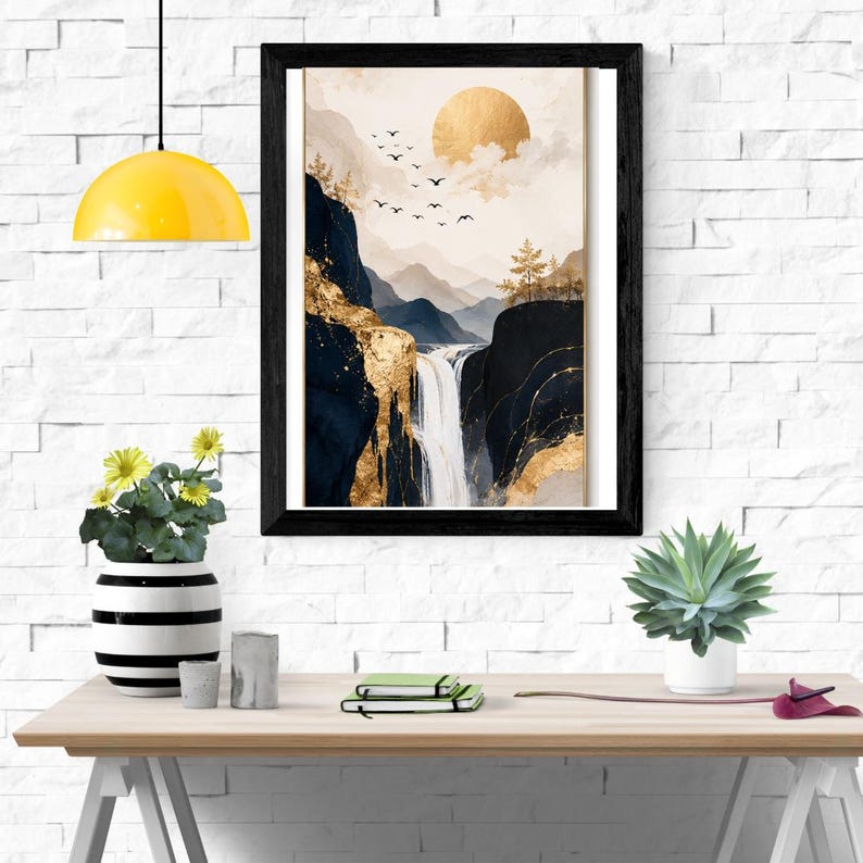 May include: A framed wall art print featuring a landscape with a waterfall, dark blue mountains, and a golden sun. The artwork includes gold leaf accents, silhouettes of birds in flight, and sparse trees against a soft, neutral-toned sky background.