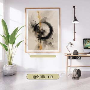 Op de afbeelding: Een ingelijste kunstdruk met een abstracte zwarte inktcirkel op een beige achtergrond met een verticaal bladgoud accent. Het kunstwerk toont spetters en aquarelachtige wassingen in grijstinten en zwart, ingesloten in een lichthouten lijst.
