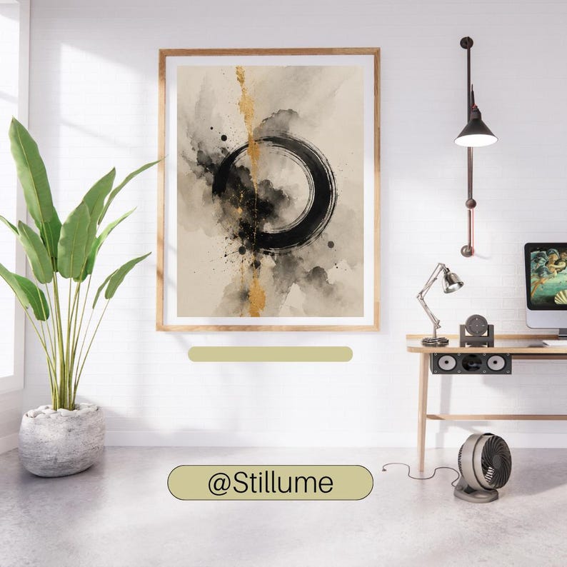 Op de afbeelding: Een ingelijste kunstdruk met een abstracte zwarte inktcirkel op een beige achtergrond met een verticaal bladgoud accent. Het kunstwerk toont spetters en aquarelachtige wassingen in grijstinten en zwart, ingesloten in een lichthouten lijst.