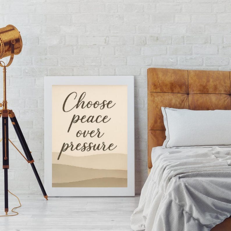 May include: A framed print with the words "Choose peace over pressure" in a stylish font. The artwork features a beige background with a minimalist landscape design in shades of brown. The frame is white.