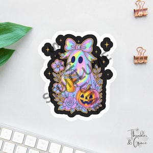 May include: A holographic sticker featuring a ghost with a large bow, holding an iced coffee drink. The ghost is surrounded by purple and blue flowers, a jack-o'-lantern, and small stars against a black background with a white border.