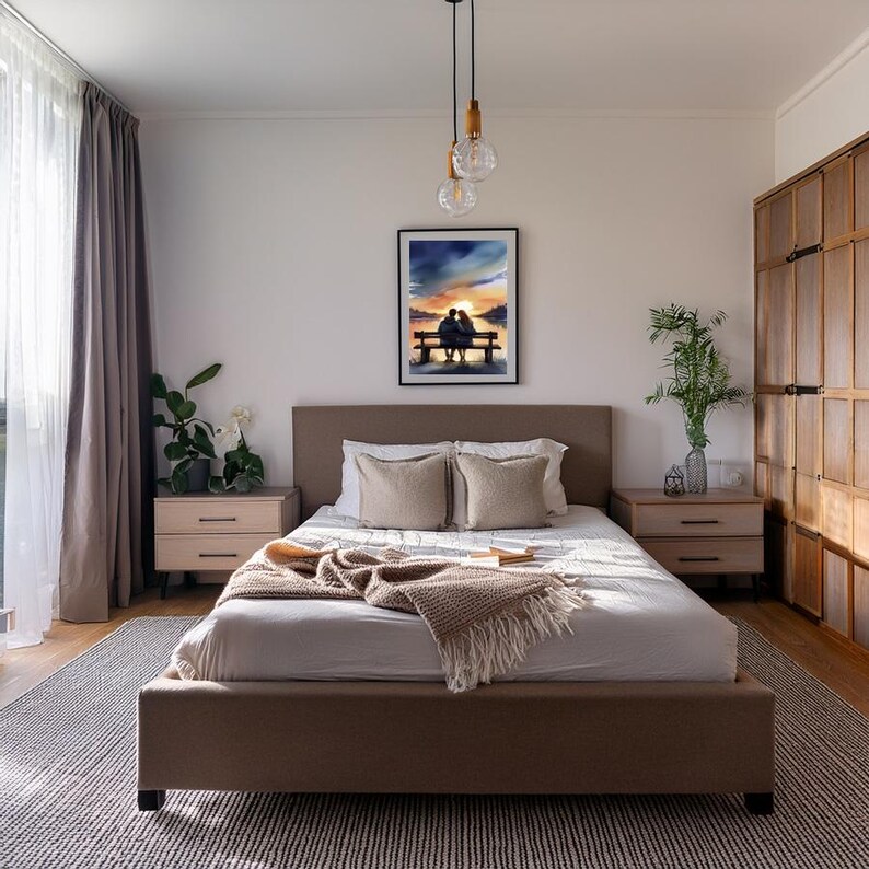 May include: A bedroom featuring a brown upholstered bed with beige pillows and a tan blanket. A framed watercolour painting of a couple on a bench at sunset hangs above the bed. Two bedside tables and a wooden wardrobe are also visible.