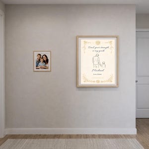 K&ouml;nnte beinhalten: Zwei gerahmte Drucke h&auml;ngen an einer hellgrauen Wand. Einer ist ein Familienportr&auml;t, der andere zeigt eine Strichzeichnung eines Vaters und Kindes mit dem Text "Papa, deine St&auml;rke ist mein Wegweiser" und dem Namen "Michael".