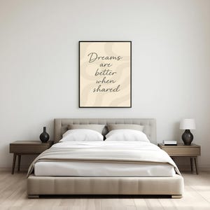 May include: A bedroom scene featuring a bed with white bedding, a beige headboard, and two nightstands. A framed print with the text "Dreams are better when shared" hangs above the bed. Decorative black vases and a lamp are on the nightstands.
