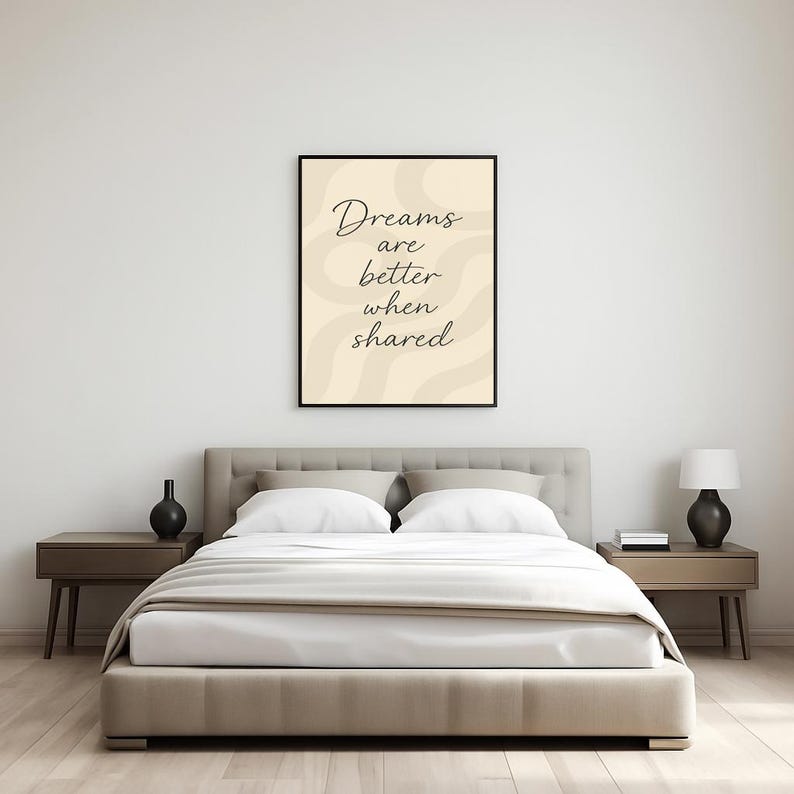 May include: A bedroom scene featuring a bed with white bedding, a beige headboard, and two nightstands. A framed print with the text "Dreams are better when shared" hangs above the bed. Decorative black vases and a lamp are on the nightstands.