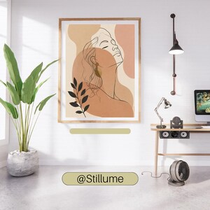 May include: A framed wall art print featuring a black line drawing of a person's profile against abstract shapes in shades of beige, tan, and terracotta. The artwork includes a black botanical illustration of leaves and the text @Stillume.