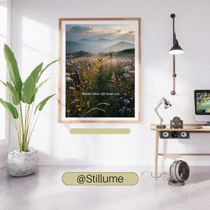 May include: A framed wall art print featuring a landscape of a wildflower meadow at sunset with distant mountains and a butterfly. The text "Bloom where life leads you." is centered in the image. The print is displayed in a wooden frame.