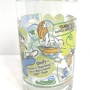 May include: Clear glass featuring Disney characters and text. The glass has images of Simba, Goofy, and other characters. Text includes "SIMBA is the Swahili word for lion" and "Goofy - first known as 'Dippy Dawg' - stars in 'Mickey's Jammin' Jungle' Parade."