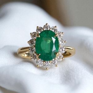 Puede incluir: Anillo de oro con una esmeralda ovalada rodeada por un halo de diamantes. La esmeralda es de color verde vibrante, y los diamantes brillan. Una joya atemporal, ideal para ocasiones especiales. Diseño clásico.