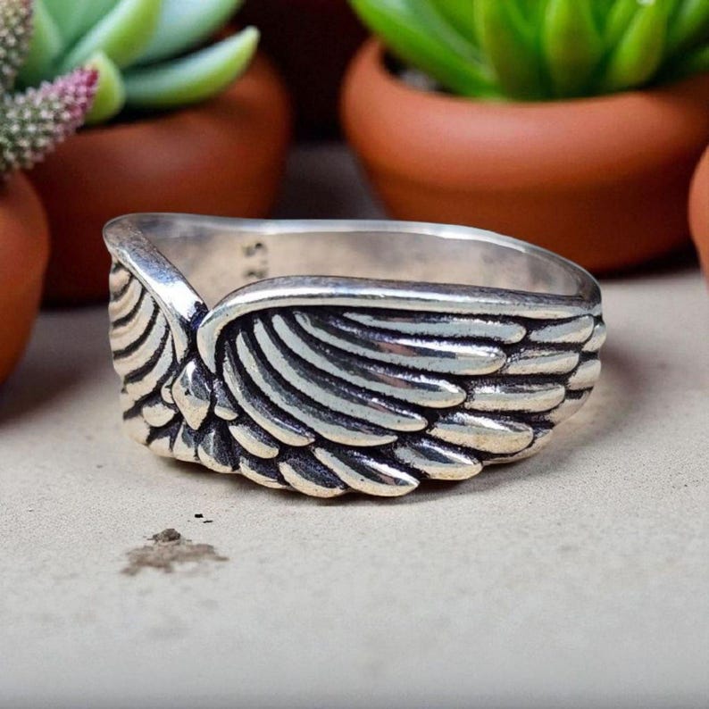 Op de afbeelding: Een zilveren ring met een gedetailleerd vleugelontwerp. De ring heeft een getextureerd oppervlak met individuele veerd details. De vleugel wikkelt zich om de band, waardoor een uniek en symbolisch sieraad ontstaat.