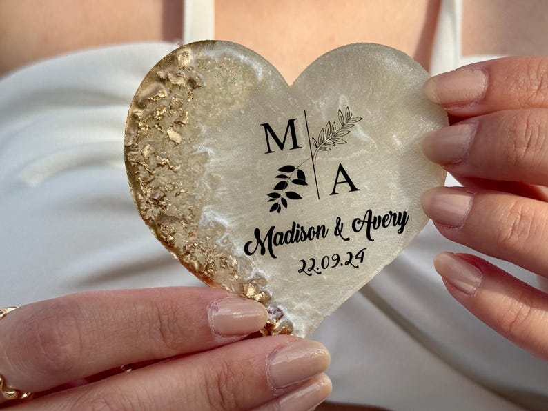 May include: Heart-shaped coaster with a gold leaf design and the names "Madison & Avery" with the date "22.09.24" printed in black. The coaster has a white and gold color scheme.