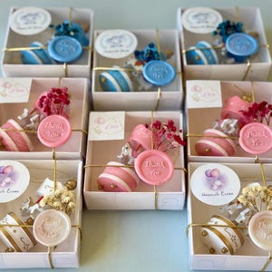 May include: A collection of seven square white gift boxes, each containing a small carousel-themed favor. The favors include a miniature carousel, dried flowers, and a wax seal stamped with the words Thank You, all tied with gold string.
