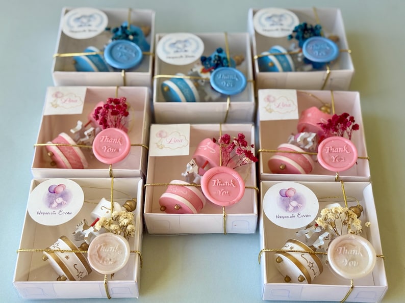 May include: A collection of seven square white gift boxes, each containing a small carousel-themed favor. The favors include a miniature carousel, dried flowers, and a wax seal stamped with the words Thank You, all tied with gold string.