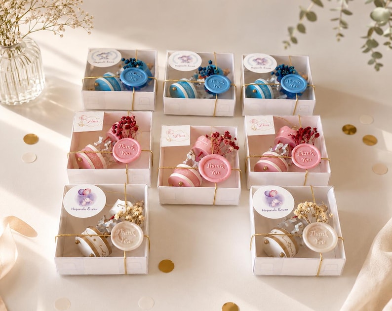 May include: A collection of seven square white gift boxes, each containing a small glass bottle with dried flowers and a wax seal stamped with the words Thank You. The boxes are arranged in three rows, featuring blue, pink, and white color themes.