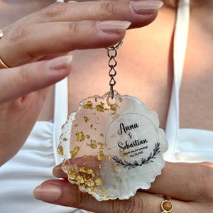 May include: A circular resin keyring with a wavy edge, featuring a white and translucent pink marbled design with embedded gold leaf flakes. The keyring includes black printed text that reads Anna & Sebastian, Thank you for coming!, Sep 28, 2025, and a decorative leaf motif.