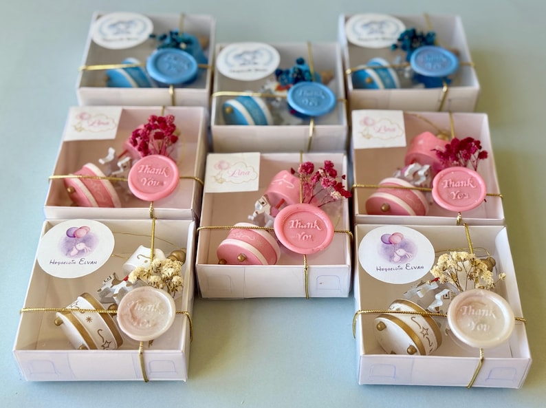 May include: A collection of square white gift boxes containing small round containers, dried flowers, and a wax seal stamped with the words Thank You. The boxes are tied with gold string and feature circular labels with various illustrations.