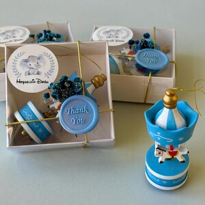 May include: Two white square gift boxes containing blue and white carousel ornaments with gold accents, blue dried flowers, and a light blue wax seal with the text Thank You. A matching carousel ornament stands outside the boxes.