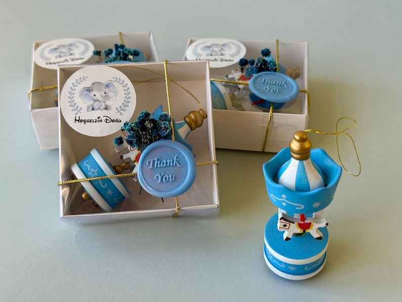 May include: Two white square gift boxes containing blue and white carousel ornaments with gold accents, blue dried flowers, and a light blue wax seal with the text Thank You. A matching carousel ornament stands outside the boxes.