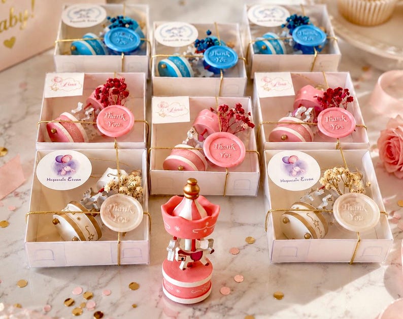 May include: A collection of square white gift boxes containing miniature carousel music boxes, each adorned with dried flowers and a wax seal stamped with the words Thank You. A single pink and white carousel music box stands in the foreground.