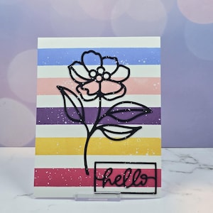 May include: A greeting card with a floral design. The card features a black outline of a flower and leaves over colorful horizontal stripes of blue, pink, purple, yellow, and red. The word "hello" is written in black script.
