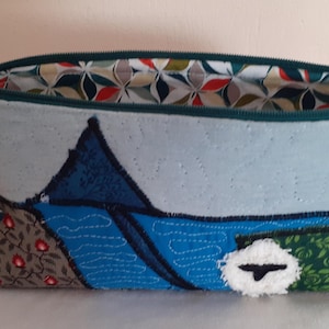 Peut inclure: Une pochette zippée ouverte faite à la main avec un motif de paysage. La pochette présente un extérieur bleu clair avec un motif patchwork de tissus bleus, verts et bruns. La doublure intérieure a un motif floral coloré. Un cordon jaune est attaché à la fermeture éclair.