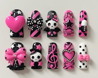 May include: A collection of press-on nails in various designs. The nails feature a black and pink color scheme with embellishments like hearts, bows, skulls, stars, and musical notes. Some nails have a glossy finish, while others have a matte appearance.