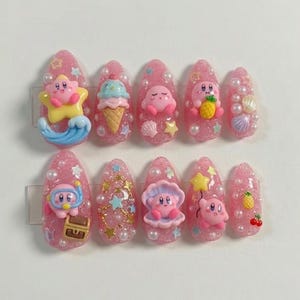 May include: Pink acrylic nail set with various 3D embellishments. Designs include a star, ice cream cone, sea shells, a treasure chest, and a character. Each nail is adorned with small pearls and glitter.