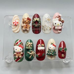 Op de afbeelding: Een set van tien kunstnagels met kerstthema's, waaronder Hello Kitty als peperkoekfiguurtje, een rood ruitpatroon met een krans, witte sneeuwvlokken, Hello Kitty met een wintermuts, zuurstokken, cadeautjes en een kerstsok.