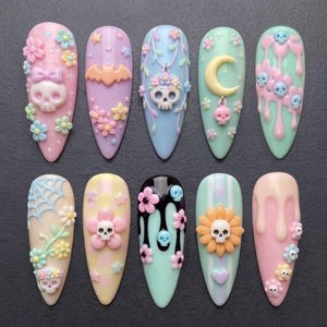 May include: Ten almond-shaped press-on nails featuring pastel-colored 3D decorations. Designs include skulls, flowers, stars, a crescent moon, a bat, spiderwebs, and dripping liquid effects in shades of pink, blue, green, yellow, and black.