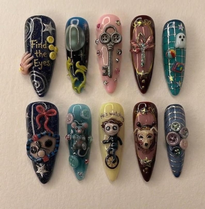 May include: A collection of ten uniquely designed, long, pointed acrylic nails. Each nail features intricate, colorful designs, including a key, a ghost, a mouse, and the text "Find the Eyes" and "He's watching". The nails are decorated with glitter, gems, and 3D elements.