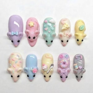 Peut inclure: Dix petits ornements pour ongles en forme de souris sculptée aux couleurs pastel. Chaque souris présente des détails en relief uniques, notamment un nœud, une étoile, des cœurs, du fromage, une feuille, des vermicelles, une rose, un cupcake avec cuillère, un donut et des accessoires de couture.